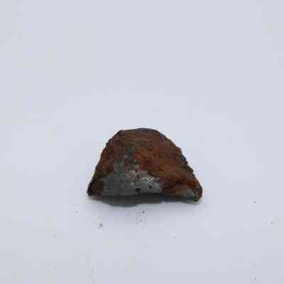 Closeup of tiny basaltic glass flake: A rough, brown basaltic glass fragment sits against a plain white background, showcasing its textured surface and natural formation.