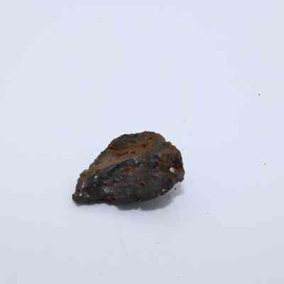 Closeup of tiny basaltic glass flake: A piece of basaltic glass with a rough, dark surface rests on a plain white background, showcasing its unique texture and color.