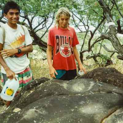 Two young people standing near a pohaku (rock)