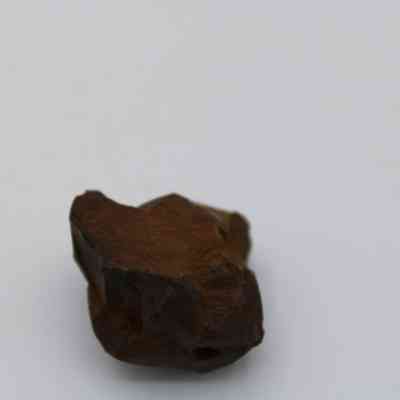 Closeup of basaltic glass core: The image shows a rugged piece of basaltic glass core, exhibiting a dark brown color with uneven, rough surfaces against a white background.