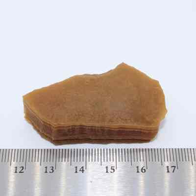Agate flake with ruler: A brown agate flake, displaying stratified layers, is positioned against a light background, next to a silver ruler for scale.