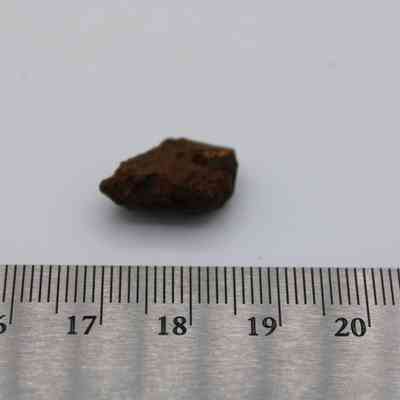Closeup of basaltic glass core with metal ruler: The image shows a small basaltic glass core placed on a white surface next to a gray ruler, indicating its size.