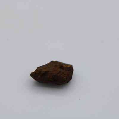 Closeup of basaltic glass core: The image shows a small, rough piece of basaltic glass, featuring a dark, irregular surface, resting on a plain white background.