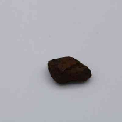 Closeup of small basaltic glass core: A small piece of basaltic glass core lies on a plain, light background, showcasing its dark, rough texture and irregular shape.
