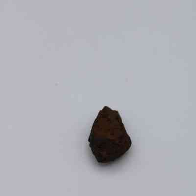 Closeup of triangular basaltic glass core: A small, dark brown, irregularly shaped rock sits prominently against a plain white background, showcasing its rough texture and natural form.