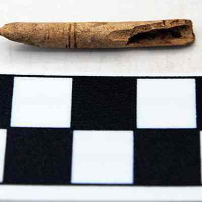 Worked bird bone with scale: The image shows an ancient, hollow bone artifact with one pointed end, placed above a black and white measurement scale marked in centimeters for size reference.