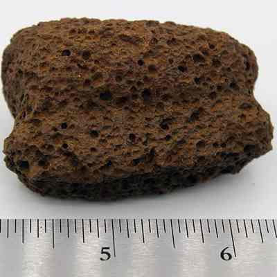 Side view of bread loaf sinker: The image features a textured, porous brown stone resembling a breadloaf sinker, placed next to a ruler for scale reference.