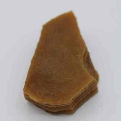 Closeup of an agate flake: An agate flake with a brown hue appears layered and translucent, showcasing its smooth texture against a plain white background.