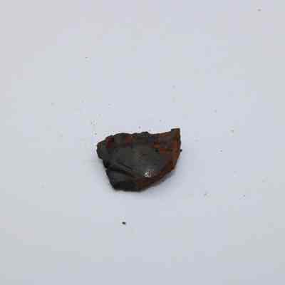 Tiny piece of basaltic glass: The image shows a small, irregularly shaped piece of basaltic glass, exhibiting a mix of dark and rusty hues, against a plain white background.
