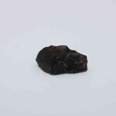 Closeup of basaltic glass flake: A small, dark basaltic glass flake lies on a plain white background with rough edges.
