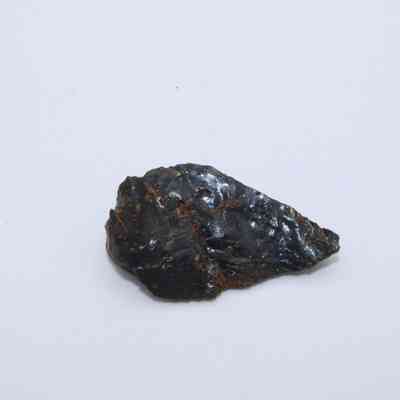 Closeup of basaltic glass flake: A small, triangular-shaped piece of basaltic glass flake lies on a flat, light-colored surface, displaying a shiny, dark exterior.