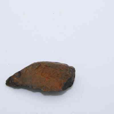 Closeup of triangular basaltic glass flake: A small, orange-hued basaltic glass flake rests on a plain white background.