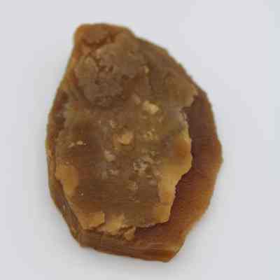 Close up lengthwise view of agate flake: The image shows a brown agate flake placed on a plain white background, highlighting its rough texture and irregular shape.