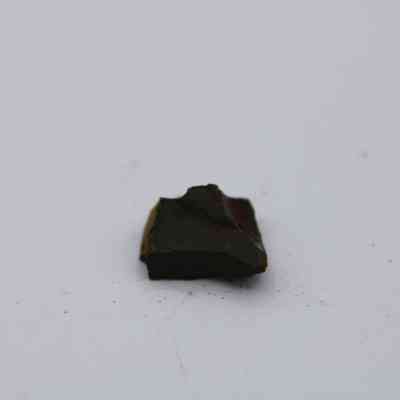 Closeup of basaltic glass core: The image features a small, dark basaltic glass core resting on a plain white surface, showcasing its rough, irregular edges and natural texture.