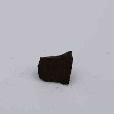 Closeup of basaltic glass core: The image shows a small, dark piece of basaltic glass core resting on a plain white surface with scattered dust particles nearby.