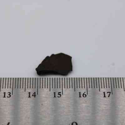 Closeup of basaltic glass flake with ruler: A small, dark basaltic glass flake is placed next to a ruler, showing its size relative to the measurement scale.