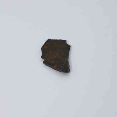 Closeup of tiny basaltic glass flake: The image depicts a small flake of basaltic glass, characterized by its dark, somewhat glossy surface and irregular, jagged edges.