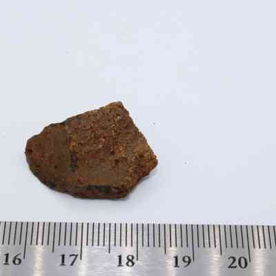 Closeup of basaltic glass core with ruler: A piece of basaltic glass core is placed alongside a ruler, providing a scale measurement on a plain white background.