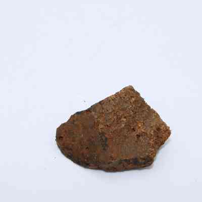 Closeup of basaltic glass core: The image shows a piece of basaltic glass core with a rugged, textured surface and uneven edges, lying on a plain white background.