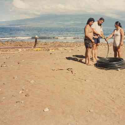 Three people working on black hose