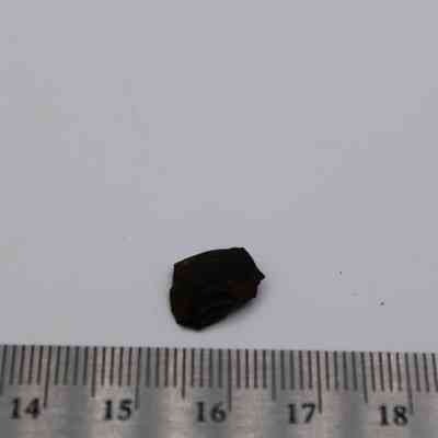 Glass flake and ruler: A small, dark glass flake is positioned on a white surface with a measuring ruler beneath, showing its tiny dimensions.