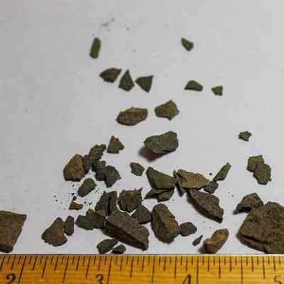 Basalt flakes: The image shows scattered brown rock fragments on a white surface, alongside a ruler indicating their small size.