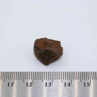 Small core of basaltic glass with metal ruler: A small piece of basaltic glass core rests on a surface near a metric ruler.