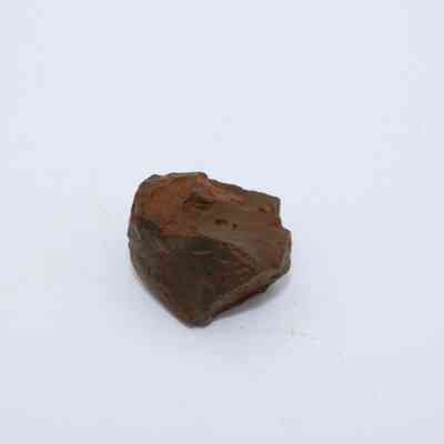 Closeup of basaltic glass core: The image shows an irregular basaltic glass core with a rough, dark surface sitting on a flat, plain background.