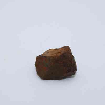 Closeup of basaltic glass core: A small piece of basaltic glass core rests on a plain white background, showcasing rough reddish and brownish textures.