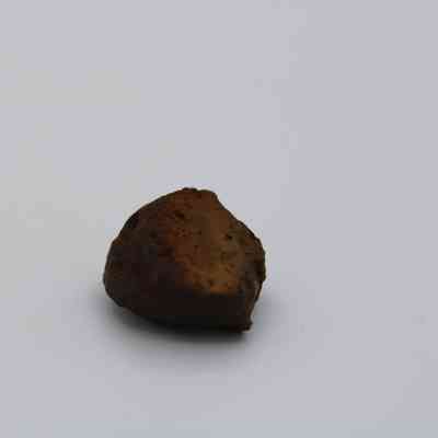 Closeup of basaltic glass core: The image shows a small, dark basaltic glass core with rough, uneven surfaces against a plain white background.
