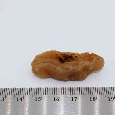 Piece of calcite with metal ruler: A calcite specimen with a rough, irregular shape is placed on a white surface alongside a metal ruler for scale reference.
