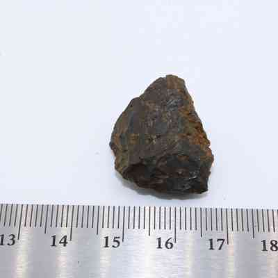 Closeup of basaltic glass and ruler: A piece of basaltic glass is shown next to a ruler for scale, highlighting its rough, irregular surface and dark coloration.