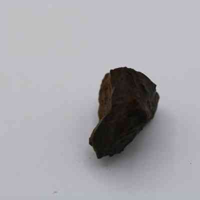 Basaltic glass: A small, dark, rough-textured piece of basaltic glass rests on a neutral, plain background, highlighting its irregular, jagged surfaces.