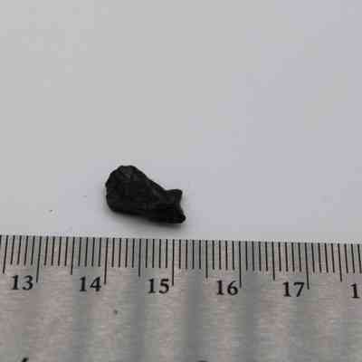 Close up of tiny basaltic glass flake with ruler: The image shows a small basaltic glass flake placed beside a ruler, highlighting its size against the scale.