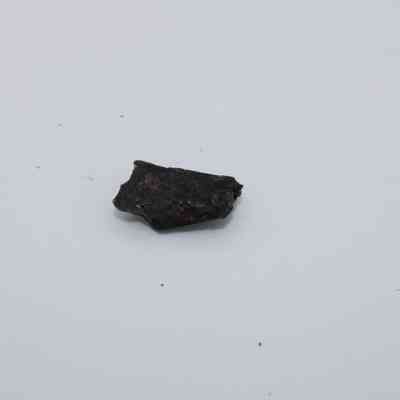 Tiny basaltic glass flake: A small, dark piece of basaltic glass flake is set against a clean, white background, highlighting its rough texture.