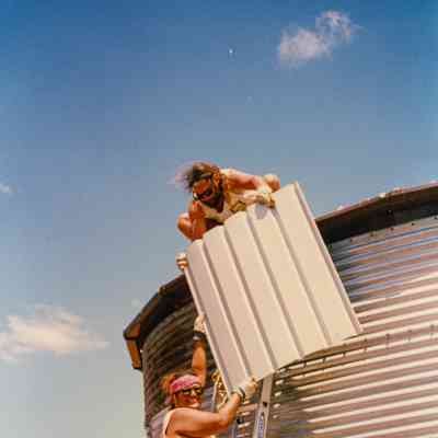 Two people put on roofing onto water tank