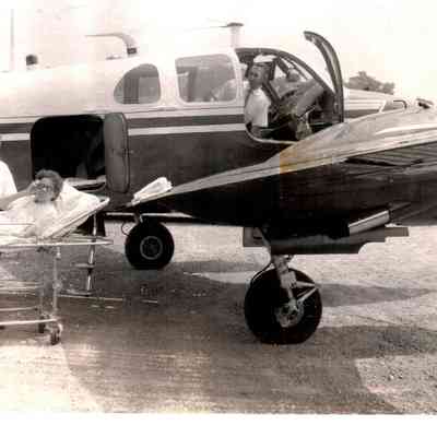 Mrs. Oscar Mills of Danville is being loaded into an airplane by J. Elmer Sims, Lee Guthrie while Vernon Record waits inside the plane. (1960)