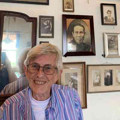 Kathy Lewis standing in front of photo wall at Bloodroot - "These pictures have been hanging on Bloodroots walls for almost 50 years now.  I’m super honored to have them there."