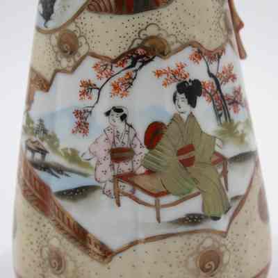Painted Japanese porcelain teapot and lid scene.: Up close image of the gold and red painted teapot with matching lid. It is decorated with an image of geisha sitting in a garden wearing pink and green kimonos under cherry blossoms.