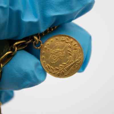 One side of a 50 Kurush gold coin.: Up close image of a 50 Kurush gold coin. There is a pair of olive branches, a cannon, and stars.
