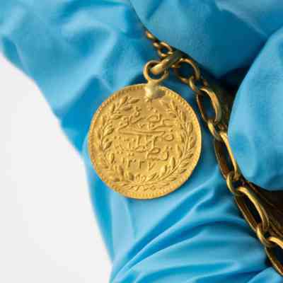 One side of a 50 Kurush gold coin.: Up close image of a 50 Kurush gold coin. There is a pair of olive branches and Arabic script.