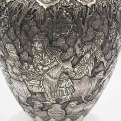 Scene on the silver and brass urn from Persia.: Up close image of the debossed scene on the silver urn. The scene depicts a woman and man with their children on a donkey. There is also a man herding an ox.