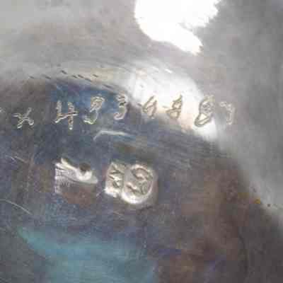 Bottom of the small sterling silver scalloped serving bowel with engravings of vines and swirls.: Up close image of the sterling silver bowl. It is engraved with "TX 4334887" and two stamped silversmith marks.