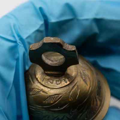 Claw bell: A hand wearing blue gloves holds a brass floral prayer bell.
