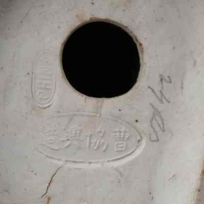 Bottom of the painted porcelain figurine of a Mongolian man and boy.: Up close image of the bottom of the porcelain figurine. It is stamped with "CHINA" and the artists name, "Created by Cao Xie Xing" in Mandarin.
