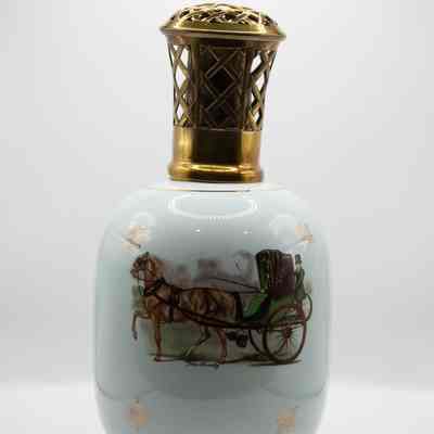 Other side of blue Lampe Berger with gold-toned top and scene of horse and carriage: A round light blue oil lamp with a gold cross-hatched top and base. The other side of the oil lamp has a horse and carriage with one horse and a driver and a person standing on the back of the carriage.