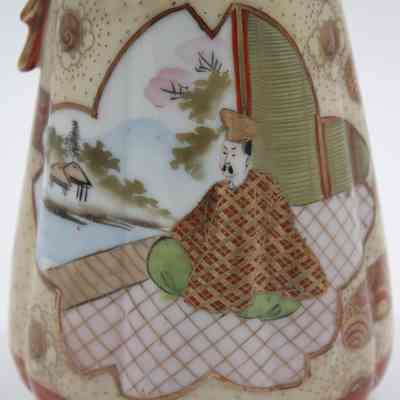 Painted Japanese porcelain teapot and lid scene.: Up close image of the gold and red painted teapot with matching lid. It is decorated with an image of a man sitting by water dressed in a red and gold top and green pants.