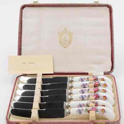 Set of Royal Crown Derby knives given to Mrs. Jessie Jordan.: Image of the set of six knives decorated with a Royal Crown Derby posies pattern. They are in a red leather case with a cream felt interior. There is a card, it reads "MRS. JORDAN." On the inside of the lid, there is a gold printed image of the seal of the Kuwait Masonic Lodge. The seal has a Kuwaiti dhow in the middle and the traditional Masonic compass at the center bottom.