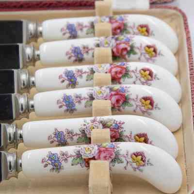 Handles of the Royal Crown Derby knives.: Up close image of the handles of the porcelain Royal Crown Derby knives. The handles are white bone China with blue, white, pink, red, and yellow flowers and green leaves.