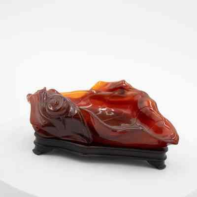 Carved amber leaf dish on wooden base.: Up close image of the red-colored carved amber dish. It is shaped like a fall leaf and rests on a dark wood ebony base.